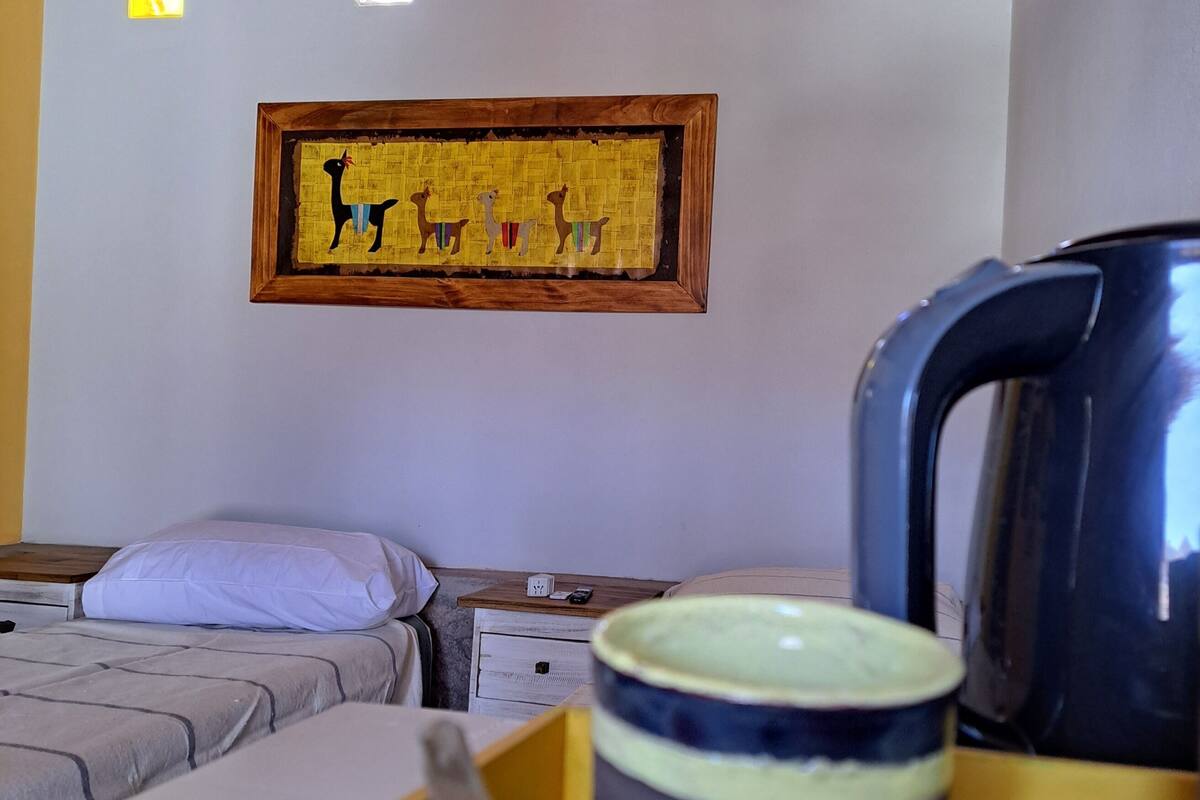 A room with a bed, a wooden nightstand, a kettle, and a framed picture on the wall.