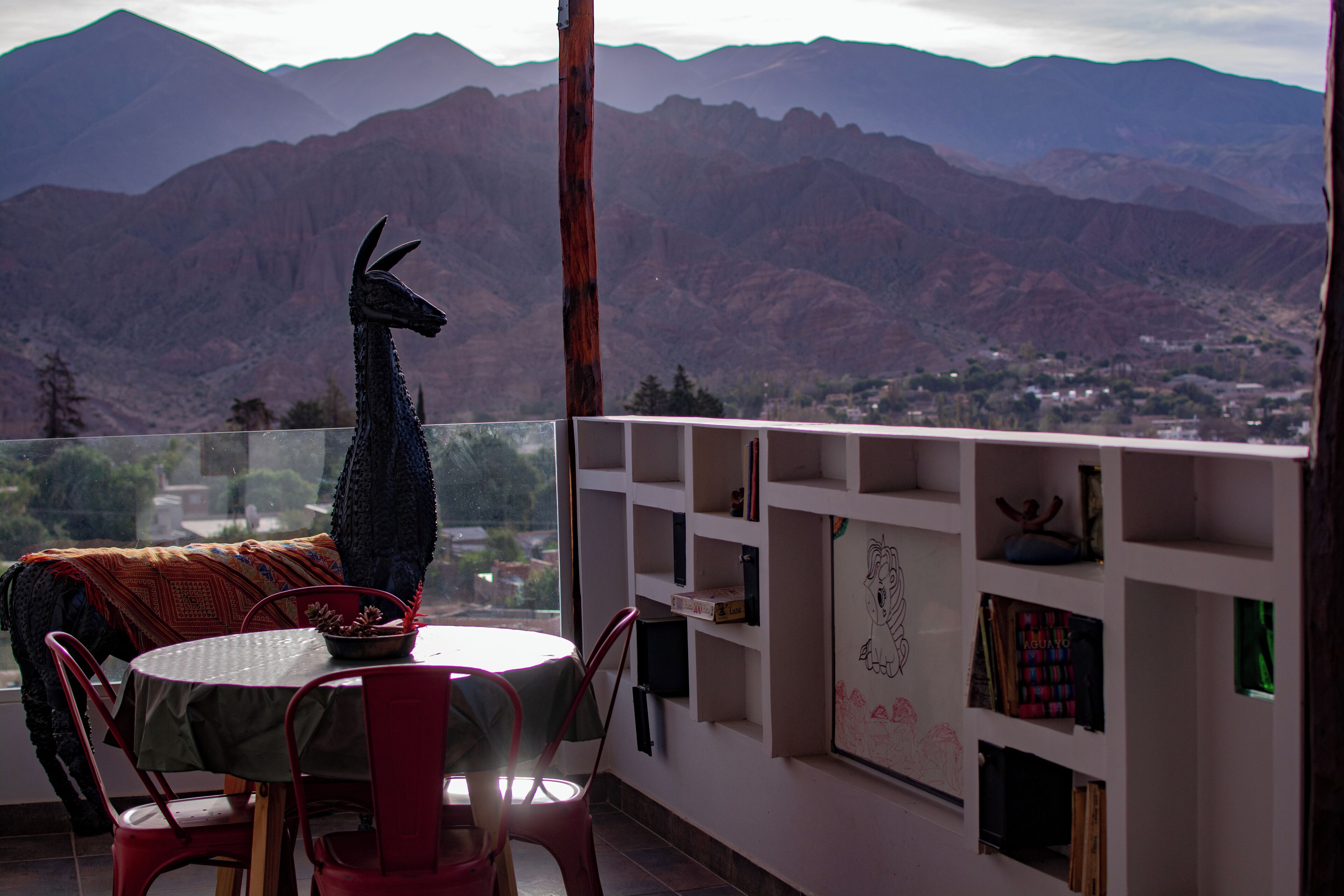 Un espace repas comprenant une table et des chaises, une sculpture décorative représentant un lama, et une vue sur les montagnes.