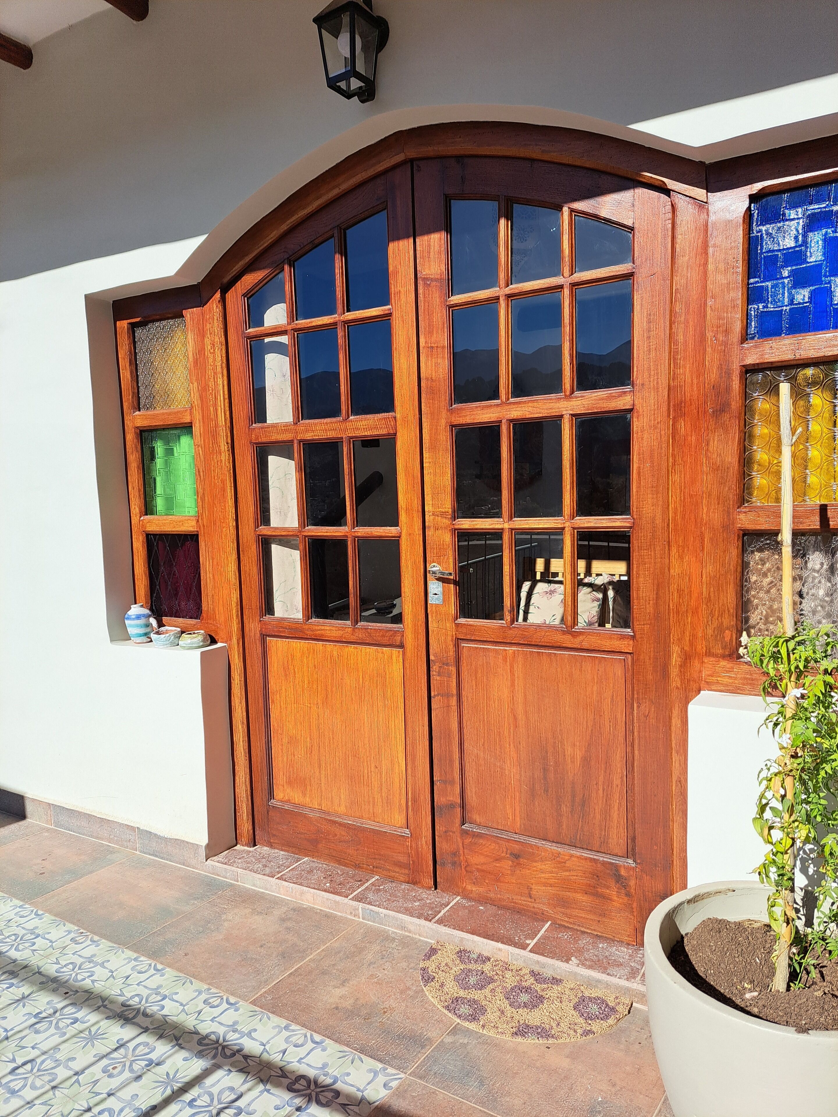 A wooden double door with multiple glass panes, a small shelf with decorative items, and a potted plant beside the door.