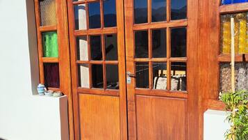 A wooden double door with multiple glass panes, a small shelf with decorative items, and a potted plant beside the door.