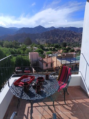 A balcony with a table set for two, a striped chair, and a view of a mountainous landscape. - La Llama Negra (Tilcara)