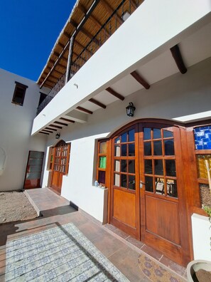 A building with a wooden door, a balcony, and a tiled entrance area. - La Llama Negra (Tilcara)