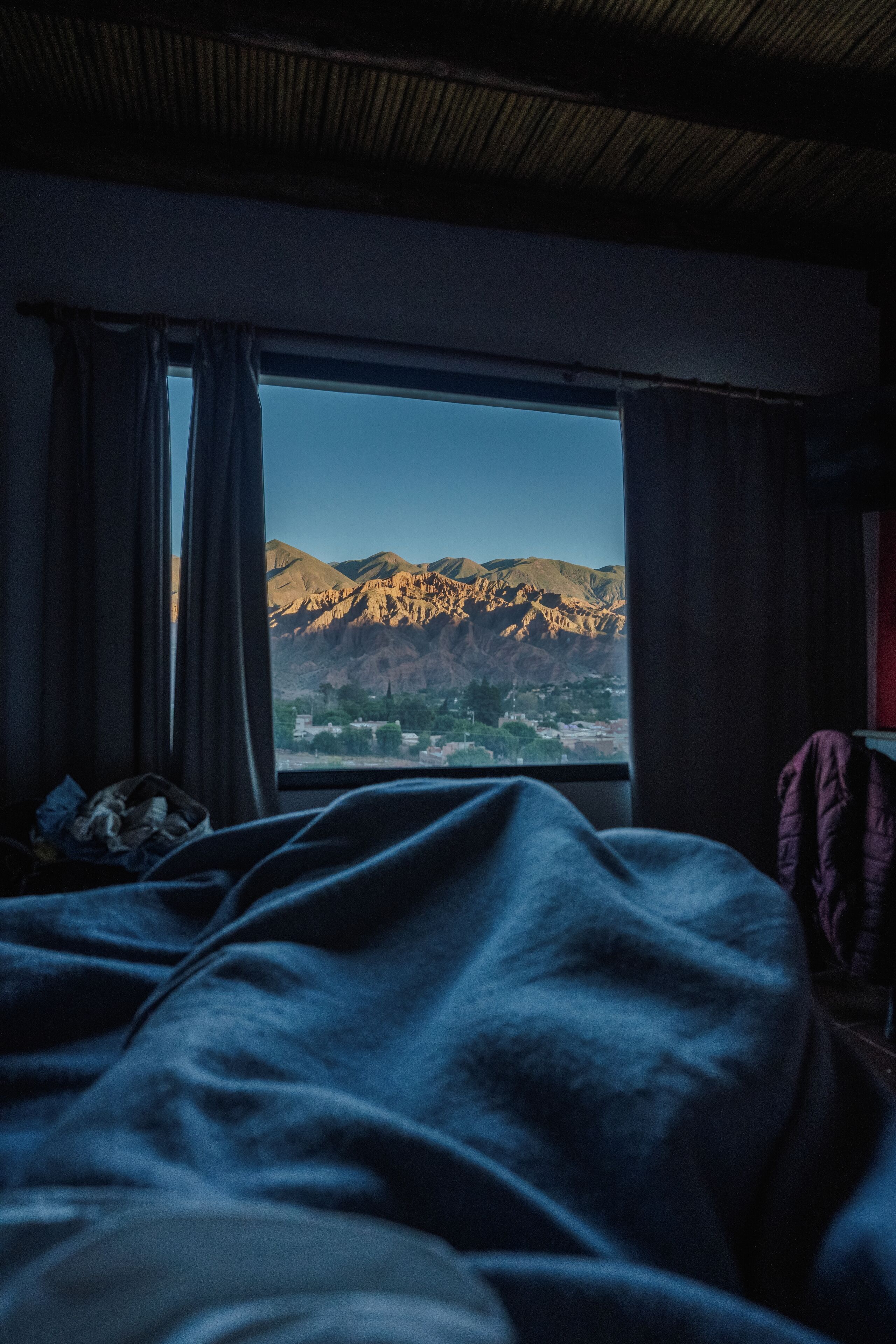 Een kamer met een bed, een raam en uitzicht op bergen.