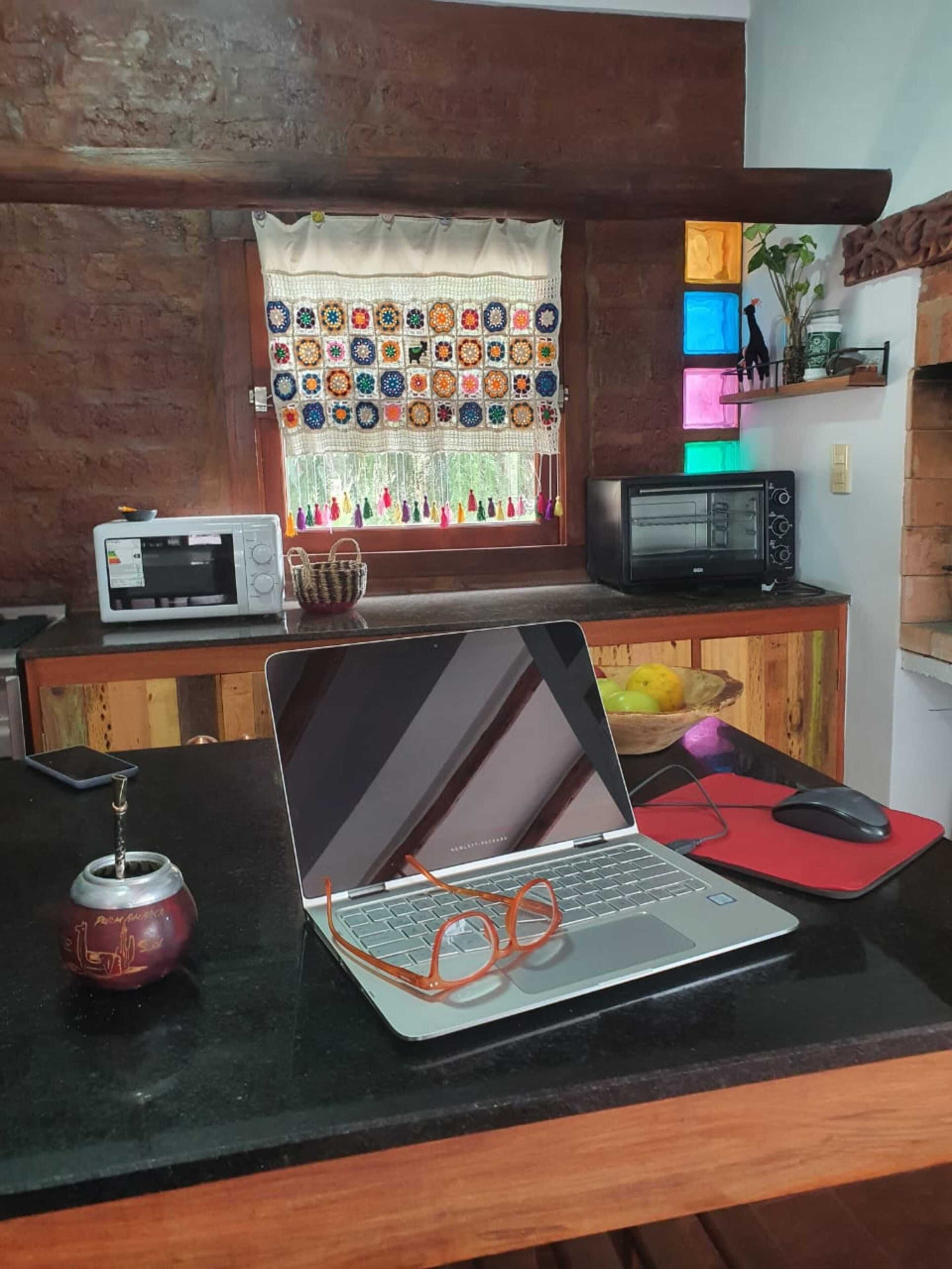 A kitchen with a microwave, a toaster, a laptop, and a red mat on the counter.