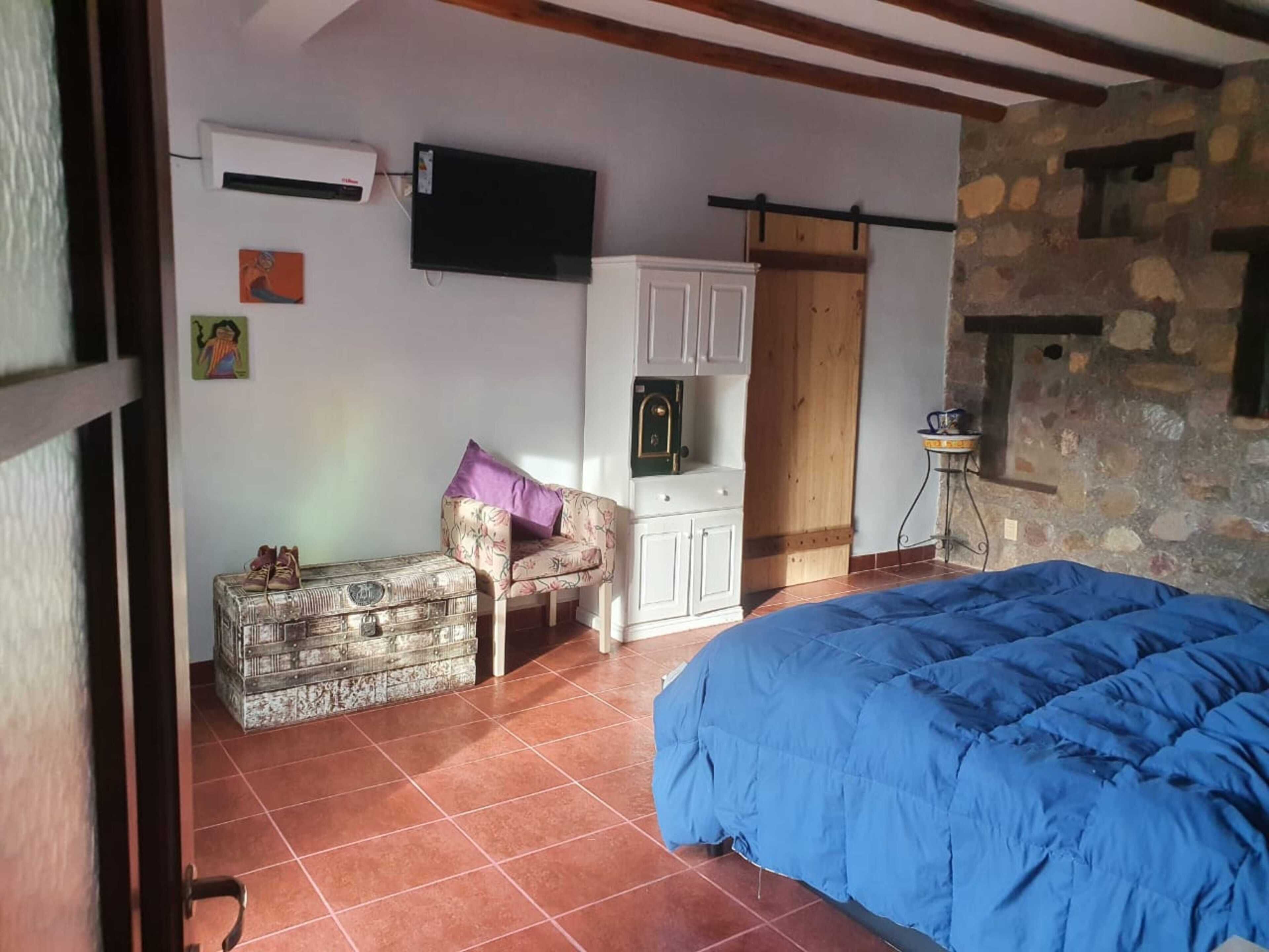 A bedroom with a bed, a chest of drawers, a chair, and a stone wall.