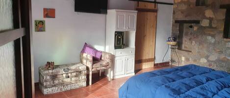 A bedroom with a bed, a chest of drawers, a chair, and a stone wall.