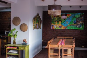 A dining area with a wooden table and benches, a hanging light fixture, and a colorful mural on the wall. - La Llama Negra (Tilcara)
