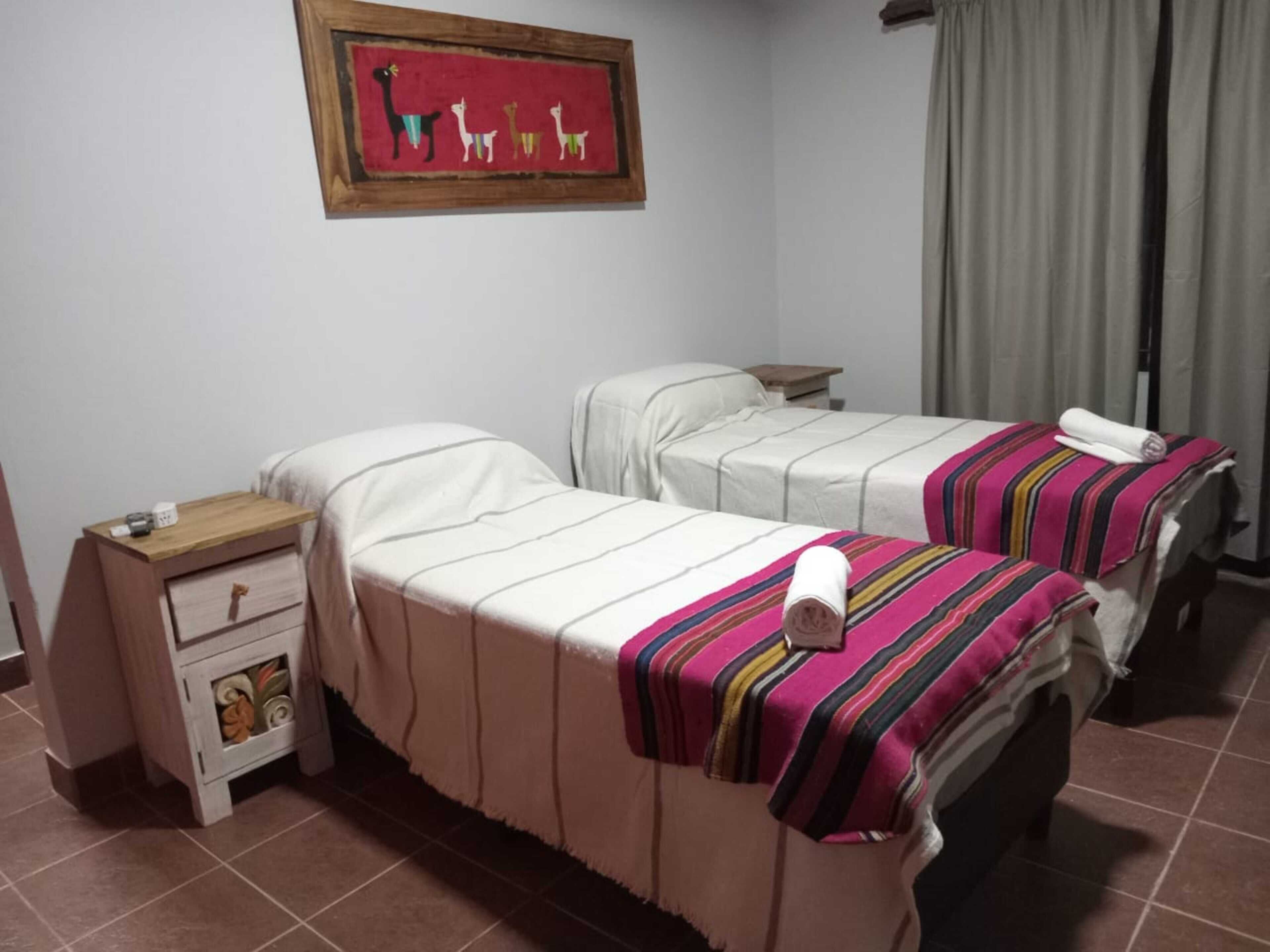 Una camera d'albergo con due letti, un comodino, un piccolo armadietto e un quadro appeso al muro.
