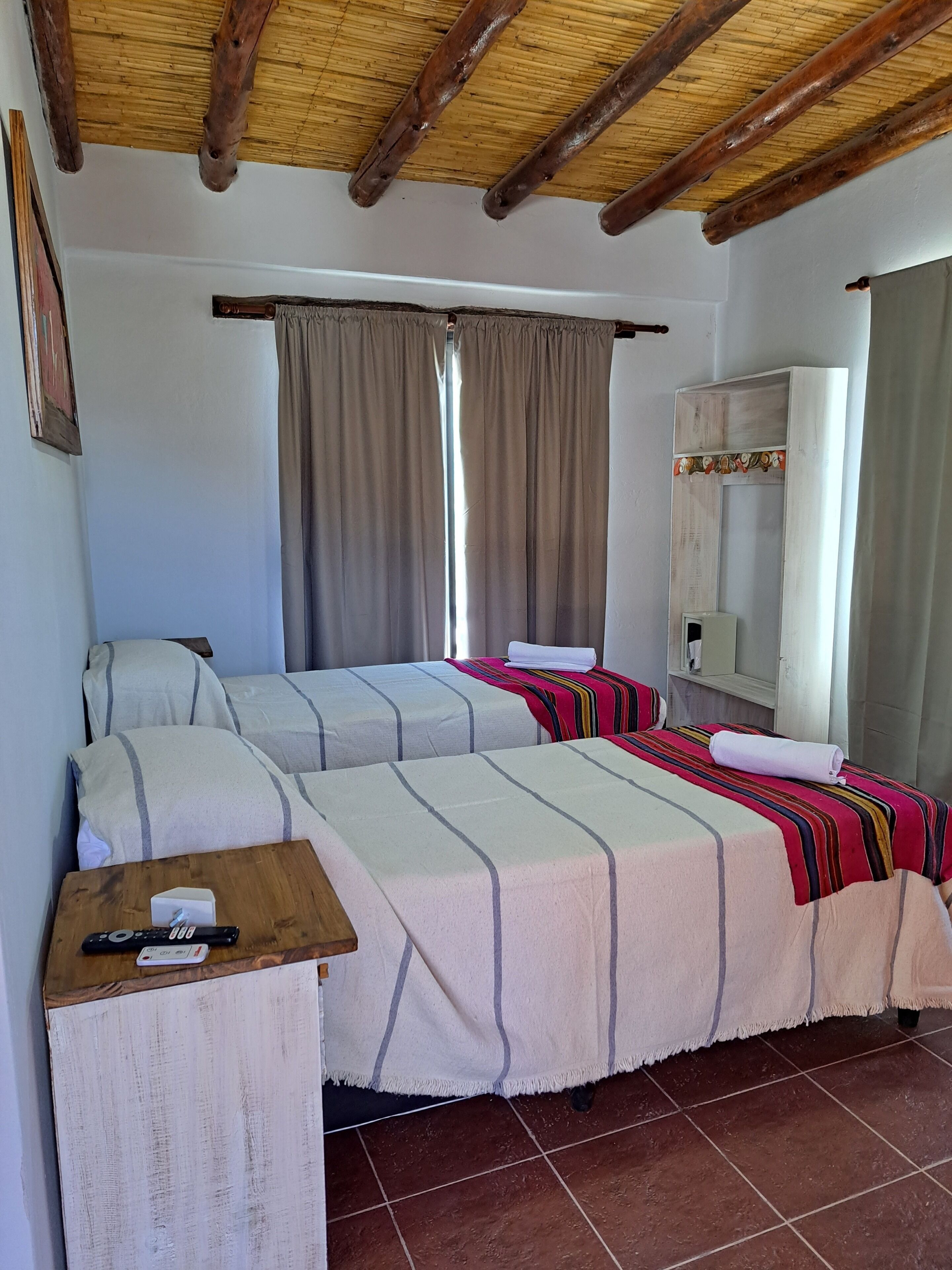 Quarto com duas camas, uma mesa de madeira com um controle remoto e um espelho na parede.