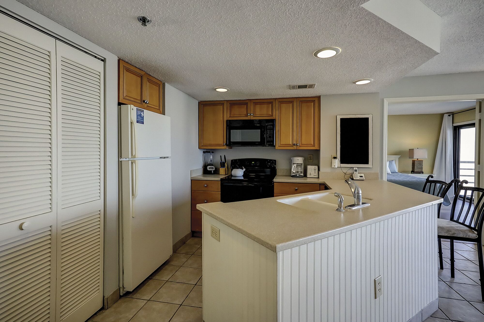 A compact kitchen with a refrigerator, microwave, stove, and sink. There is a dining area with a table and chairs.