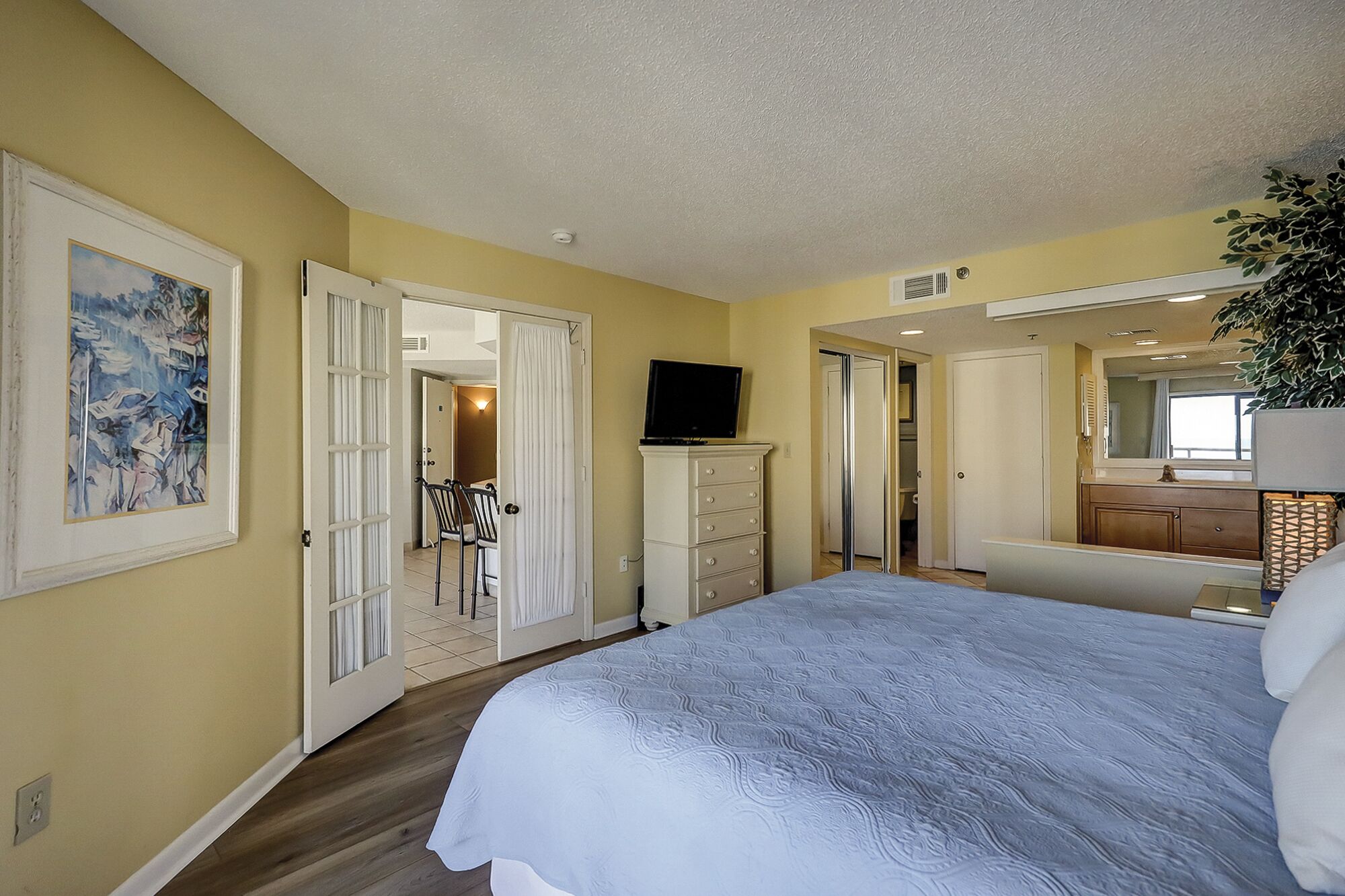 Un dormitorio con una cama, un aparador, un televisor y una puerta que da a otra habitación.
