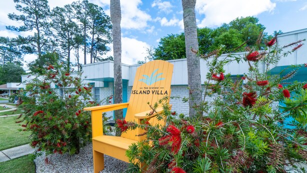 A yellow chair with a sign reading "The Iconic Island Villa" in front of a building with white walls and green trim. -  Sports Weekend Stay Near Fields, Beach & Pool onsite. Coffee/Wine in backyard (Gulf Shores)