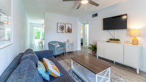 A modern living room with a sofa, a coffee table, a ceiling fan, a TV, and a small side table with a lamp. -  Sports Weekend Stay Near Fields, Beach & Pool onsite. Coffee/Wine in backyard (Gulf Shores)
