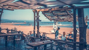 A beachside restaurant with wooden tables and chairs, a covered seating area, and a view of the beach and ocean. - Lodge Tenuta Primero in Grado (Province of Gorizia)