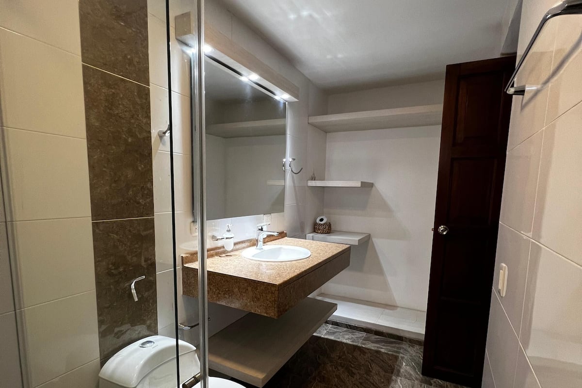 A bathroom with a glass-enclosed shower, a toilet, a sink with a marble countertop, and a bathtub.