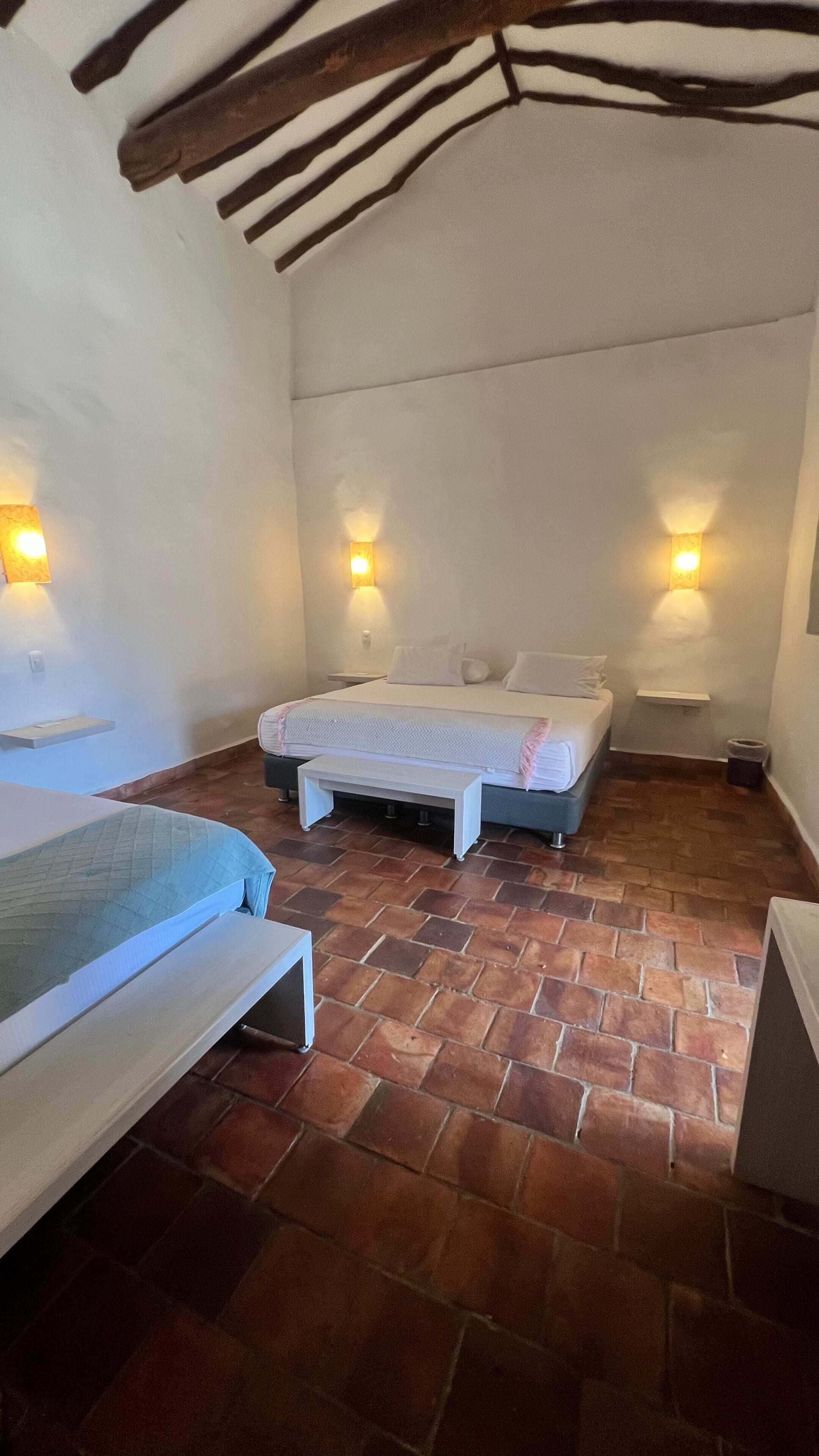 Dormitorio con dos camas, un banco y dos luces fijadas a la pared.