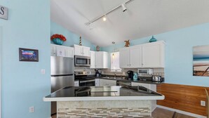 Une cuisine moderne avec des meubles blancs, un îlot central doté de sièges et une vue sur l’océan.