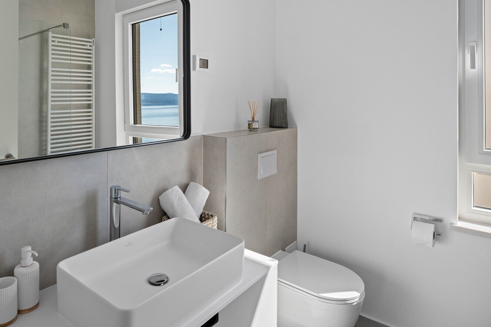 A modern bathroom with a white sink, toilet, and a large mirror.