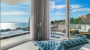 A modern living room with a large glass window, a blue sofa, and a view of the sea and buildings. - Villa Grey with 4 bedrooms, Heated pool, Sauna, Media room, Sea Views (Jesenice, Dugi Rat)