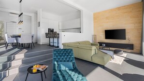 A modern living room with a sofa, a dining area with chairs, a kitchen, and a TV mounted on a wooden wall. - Villa Grey with 4 bedrooms, Heated pool, Sauna, Media room, Sea Views (Jesenice, Dugi Rat)