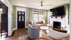 Un salon comprenant un canapé, des fauteuils, une table basse, une cheminée, un téléviseur fixé au mur et un ventilateur de plafond.