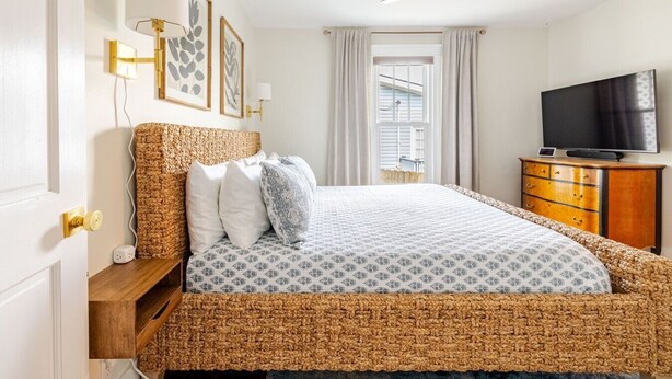 Une chambre à coucher avec un lit, une télévision, un ventilateur de plafond et une fenêtre avec des rideaux.