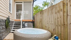 Un bain à remous dans un jardin, avec une clôture en bois, une maison et une terrasse.