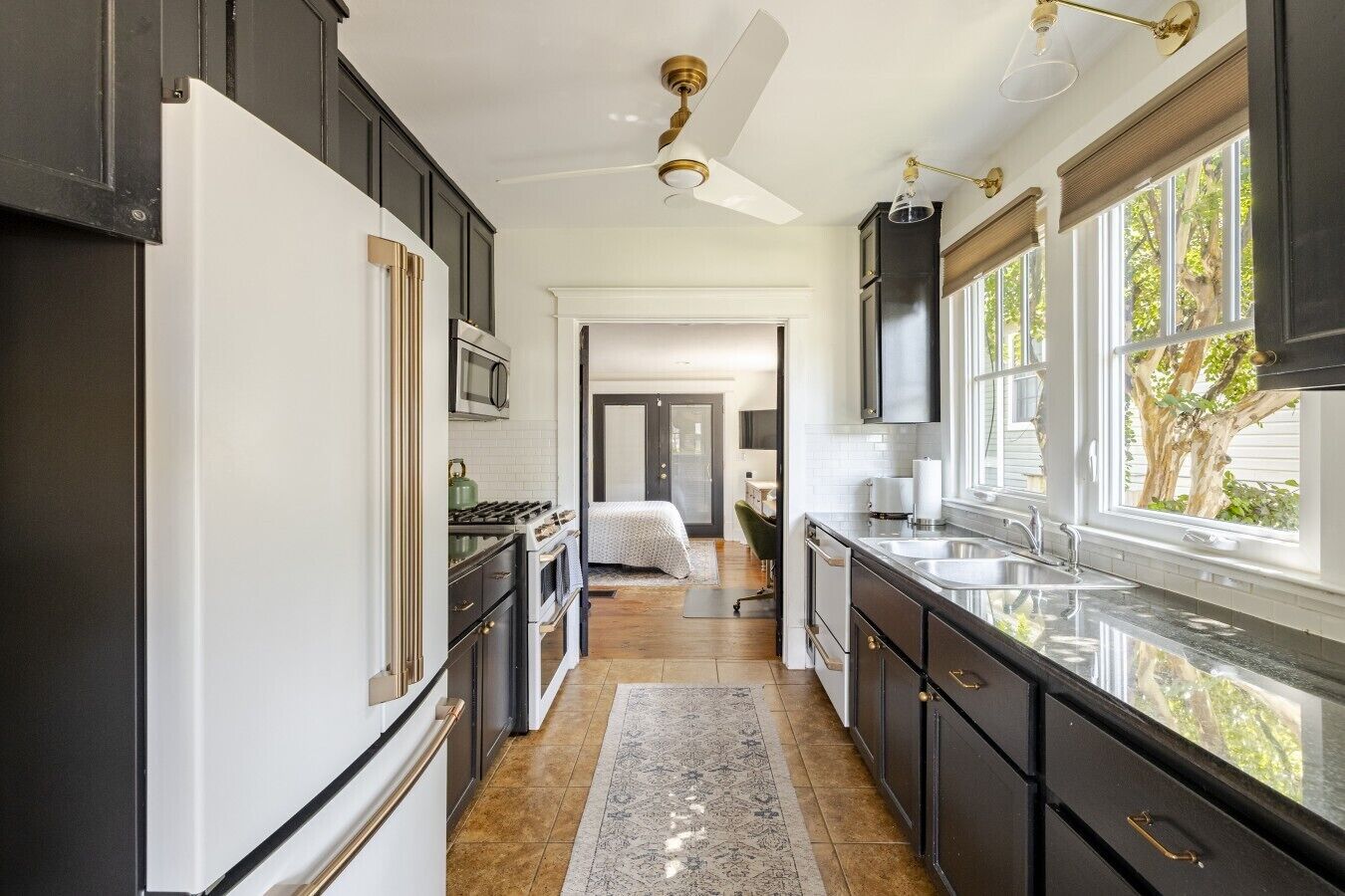 Cocina con armarios oscuros, un refrigerador blanco, una estufa y un lavamanos. Hay una ventana con vista a árboles.