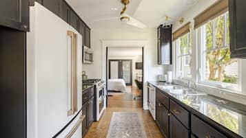 A kitchen with dark cabinetry, a white refrigerator, a stove, and a sink. There is a window with a view of trees.