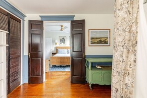 Un pasillo que conduce a un dormitorio con una cama, un aparador verde y un cuadro en la pared.