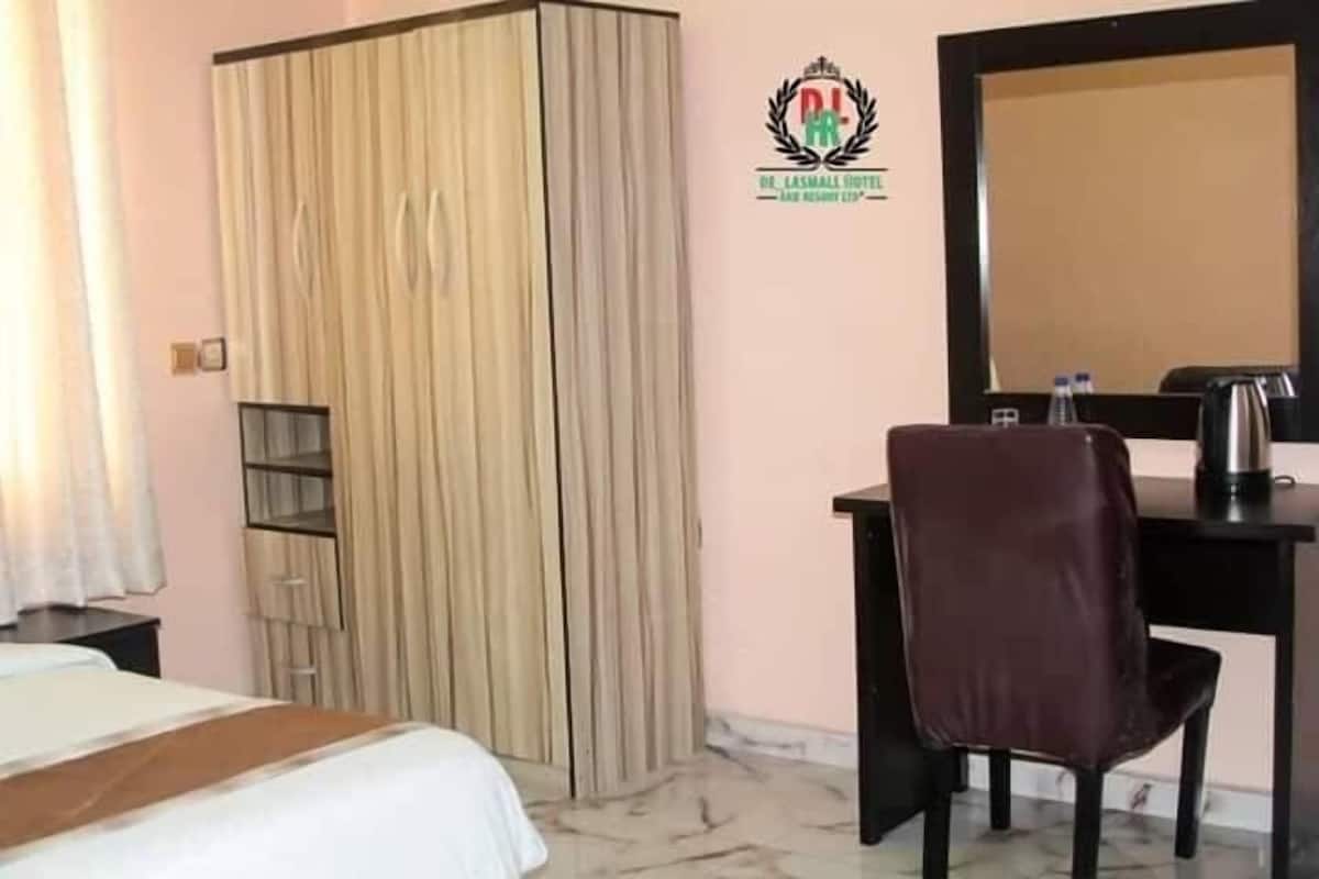 Een hotelkamer met een bed, een bureau met stoel, een kledingkast en een spiegel.