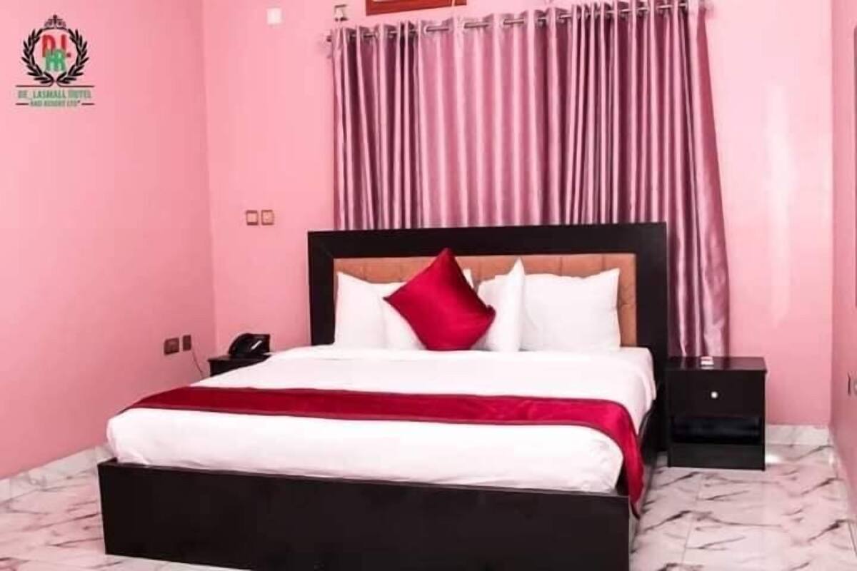 Een hotelkamer met een bed, nachtkastje en gordijn.