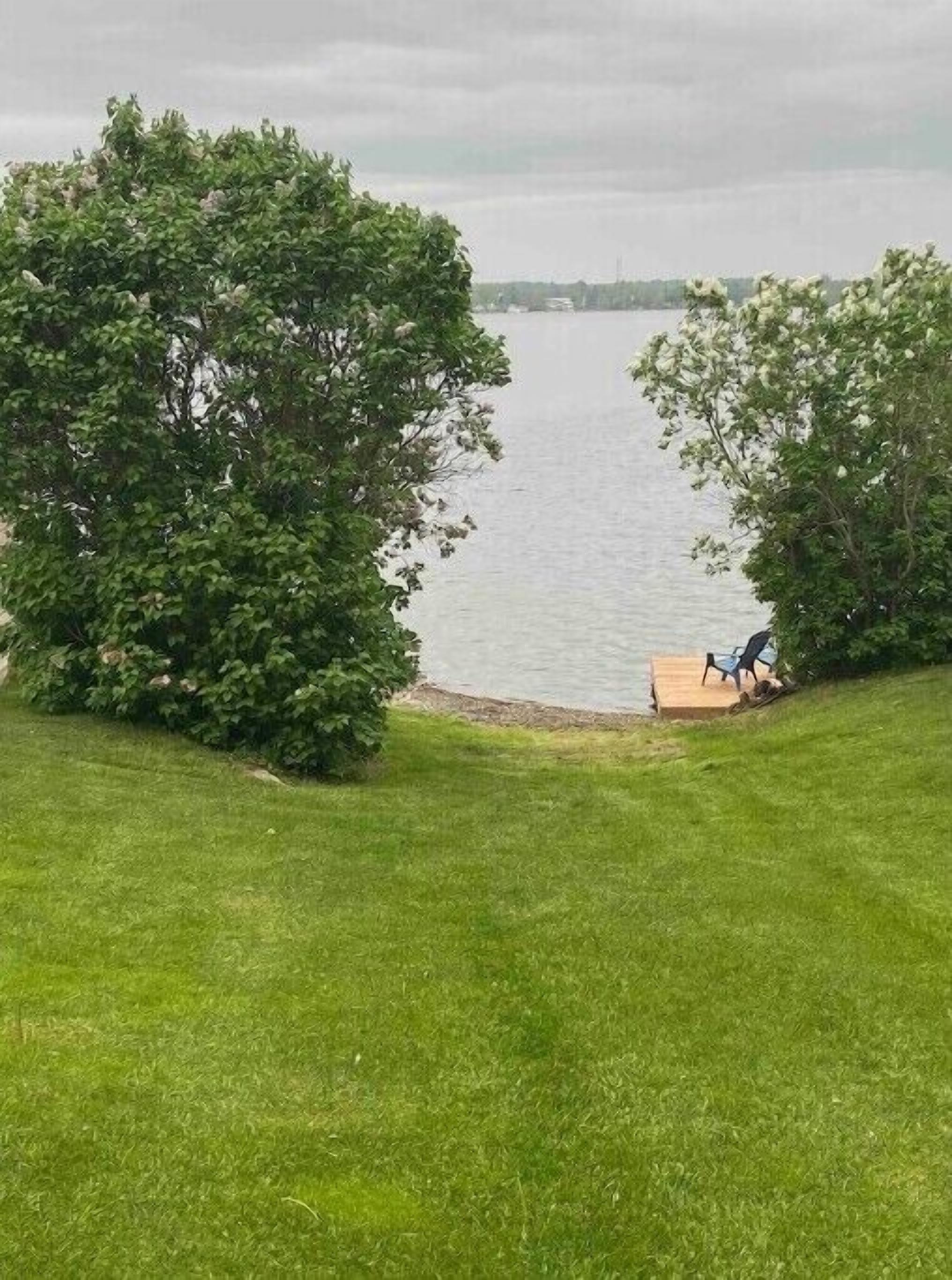A grassy area with a wooden deck and a chair overlooking a body of water.