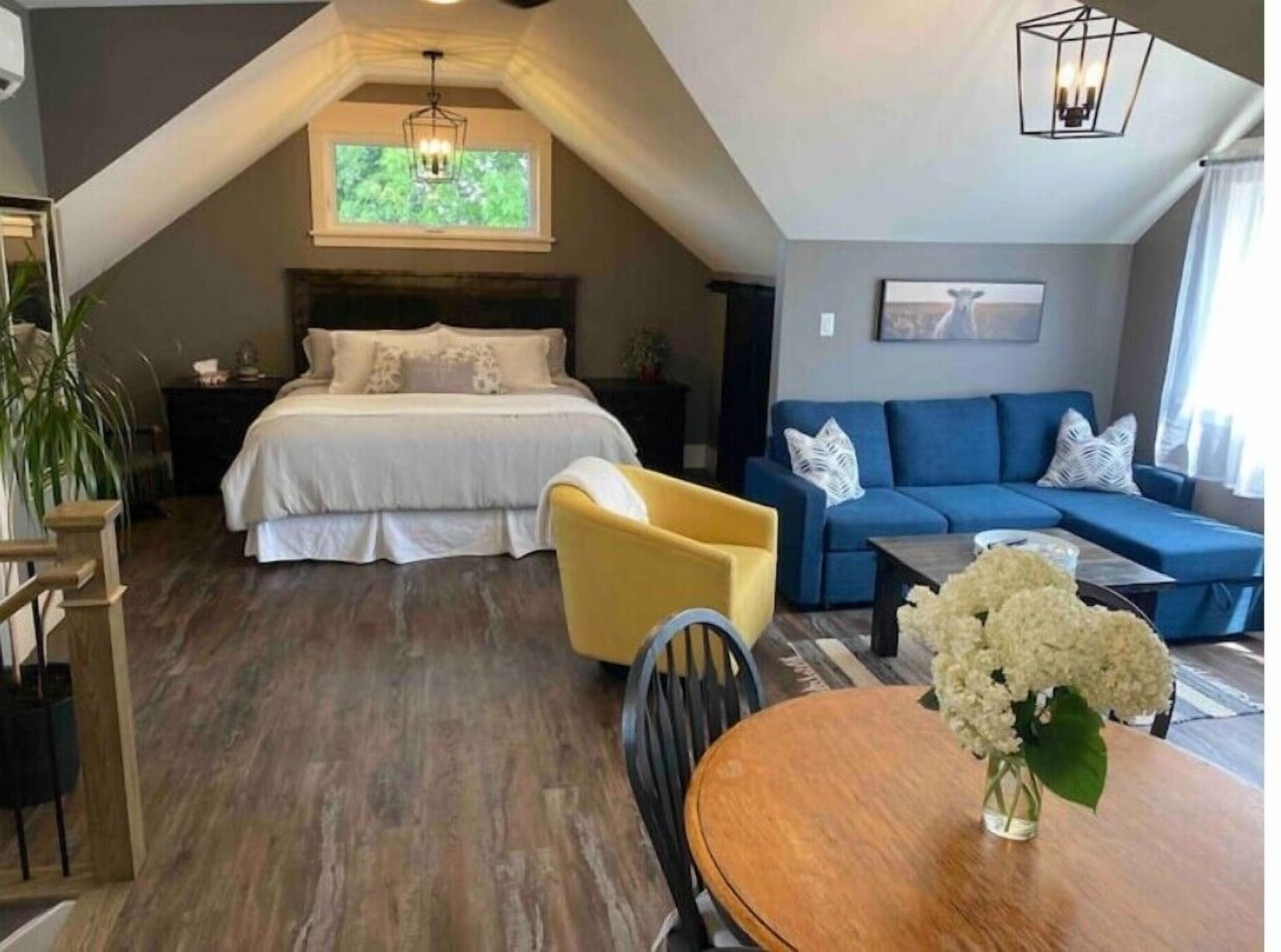 Ein Schlafzimmer mit einem Bett, einem gelben Sessel, einem blauen Sofa und einem Esstisch mit Blumen.
