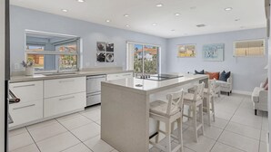 A modern kitchen with a central island, white cabinetry, and a large window providing a view of the outdoors. - RENOVATED 4/3 Canal Front, Pool and Dock (Longboat Key)