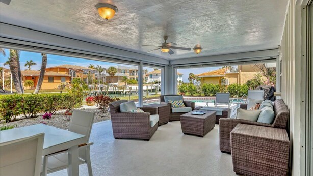 A covered outdoor lounge area with wicker furniture, a pool, and a view of a residential neighborhood. - RENOVATED 4/3 Canal Front, Pool and Dock (Longboat Key)