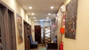 A hallway with wooden flooring, green social distancing markers, a fire extinguisher, and artwork on the walls. - Paragon Gardens & Suites (Port Harcourt)