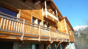 A wooden chalet with a balcony, large windows, and a stone foundation. - Appartement Plain-pied Dans Chalet, Calme, Environnement Exceptionnel (Briançon)