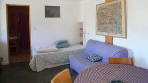 Ein kleiner, gemütlicher Raum mit einer Couch, einem Sessel und einem Tisch. Eine Tür führt in einen anderen Raum, an der Wand hängt eine gerahmte Karte.