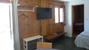 Ein Zimmer mit Holzwänden, einem an der Wand befestigten Fernseher, einer Bank, einem Tisch und einem Bett.