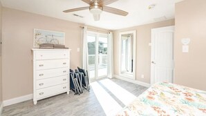 A bedroom with a ceiling fan, a dresser, a bed with a floral bedspread, and a view of the outside through a sliding door.