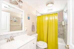 A bathroom with a white toilet, a sink with a mirror, and a shower with a yellow curtain.