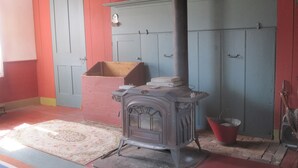 Une pièce avec un poêle d’époque, une armoire rouge et bleue et une malle en bois.