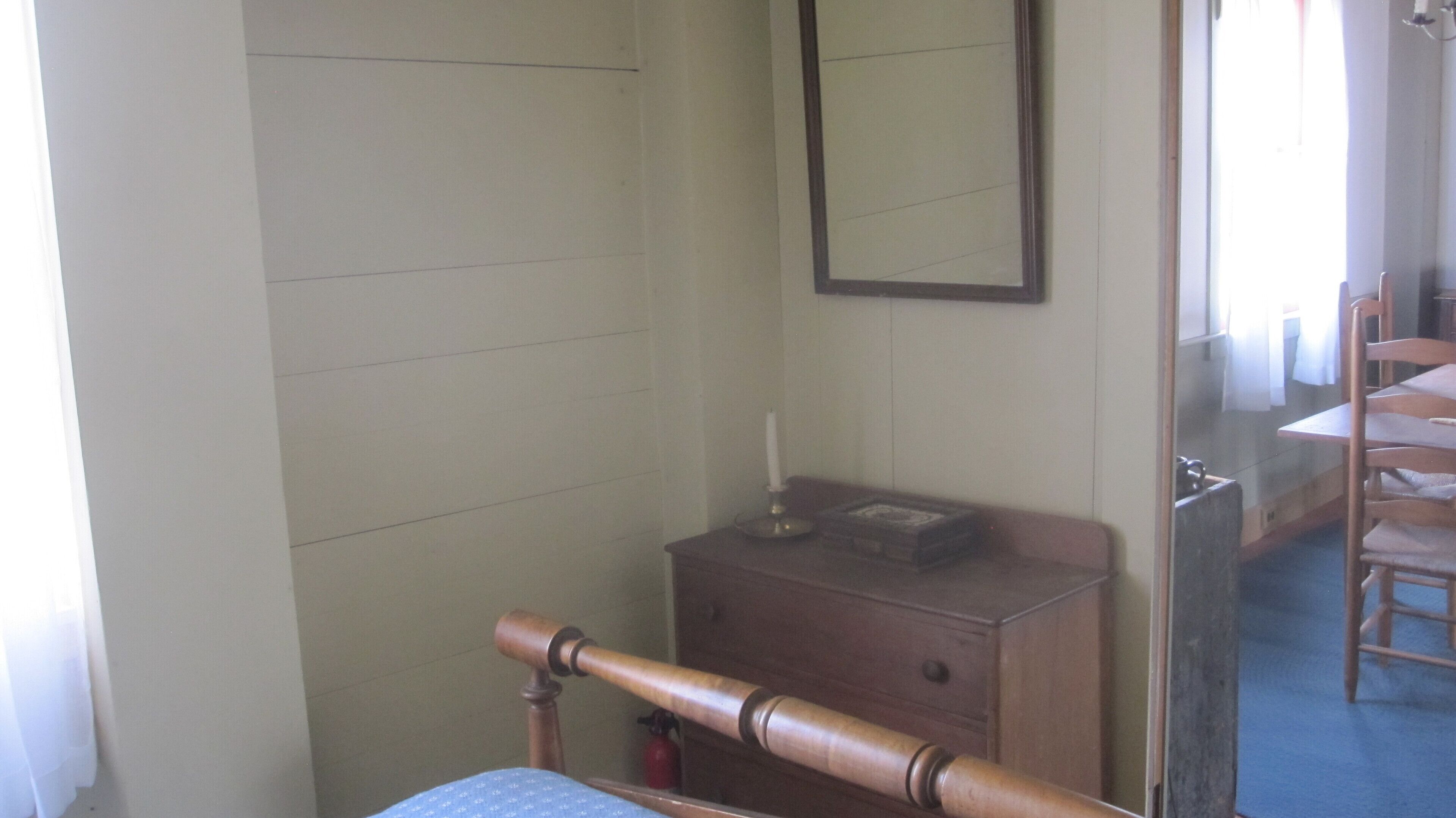 Une pièce avec une chaise en bois, une petite commode en bois et un miroir accroché au mur.