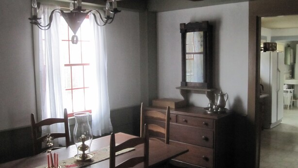 Une salle à manger comprenant une table, des chaises, un lustre, un miroir et une commode.