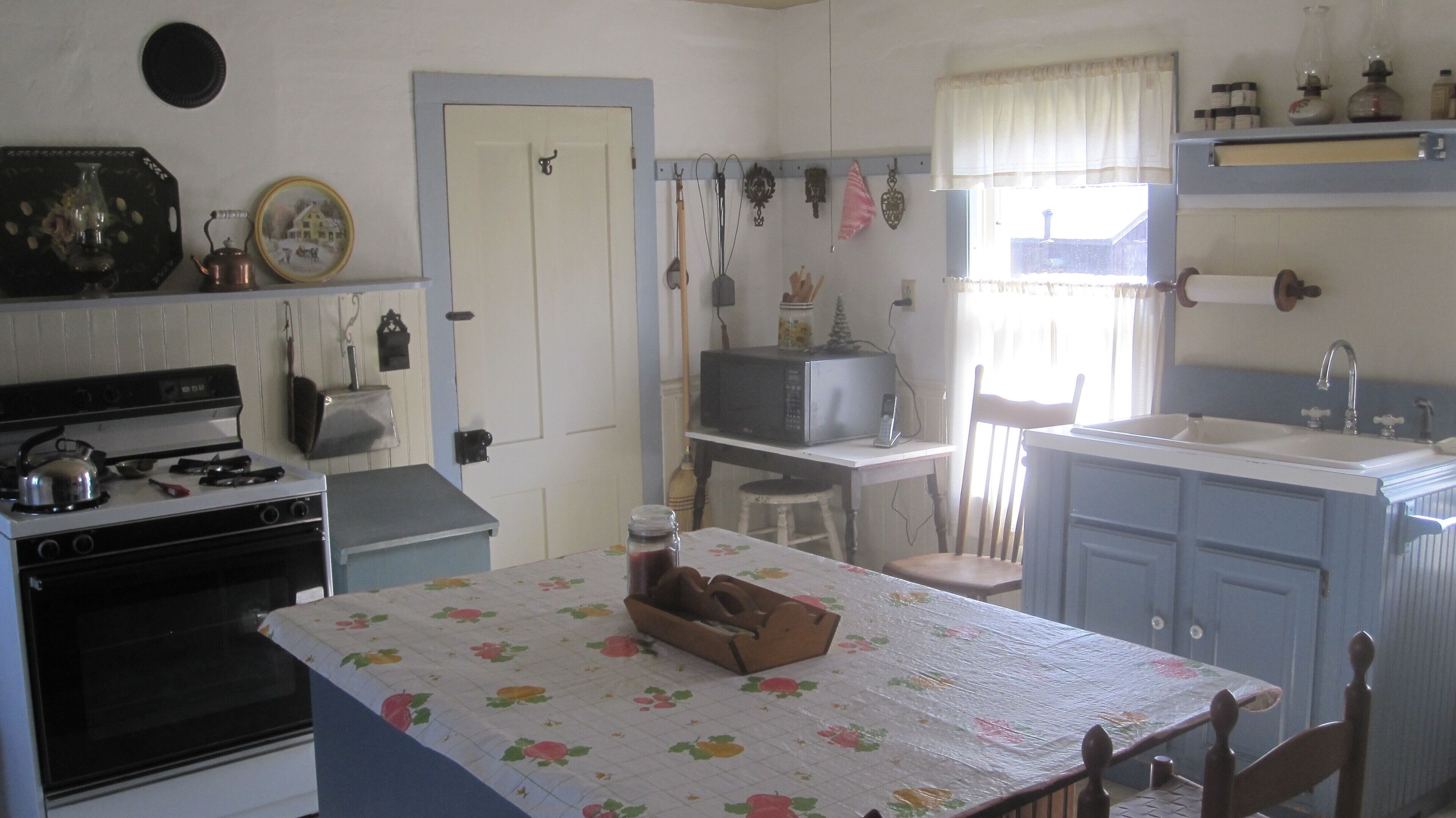 A compact kitchen with a stove, microwave, and sink. There is a table with a floral tablecloth and a box on it.