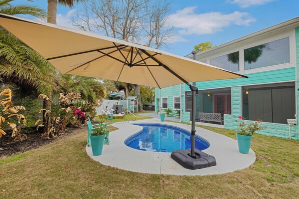 En swimmingpool med en beige parasol, omgivet af en beton terrasse og plantekasser.