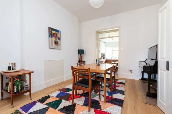 A dining area with a wooden table and chairs, a colorful rug, and a piano in the background.