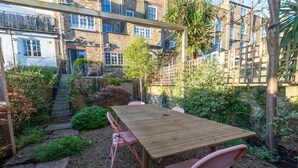 A wooden table with four chairs in a garden area with a stone pathway leading to a building with multiple windows. - Spacious 2BD Flat By Regents Park & Camden Town! (London)
