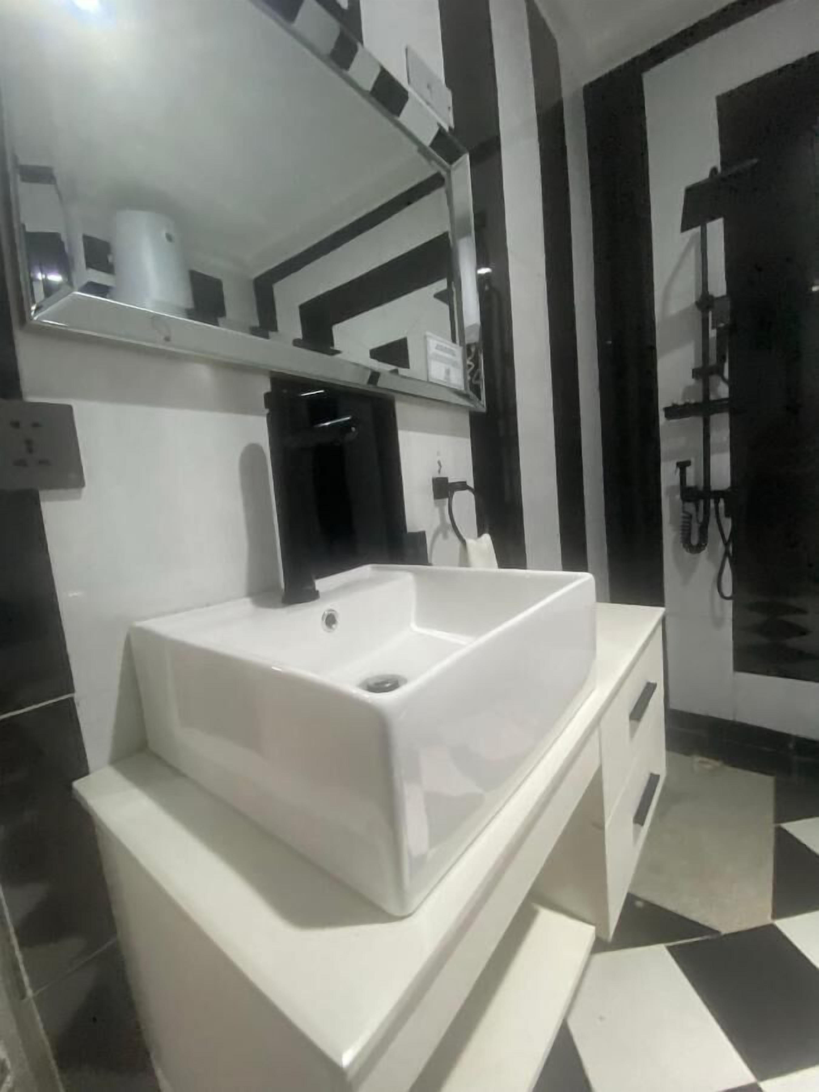 A modern bathroom with a white sink, a mirror above it, and a black and white checkered floor.